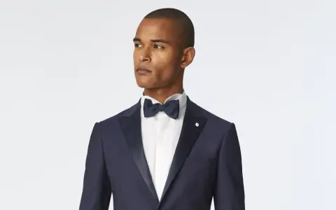 Uomo con smoking blu scuro, camicia bianca e papillon blu. Un look elegante per ogni occasione speciale.