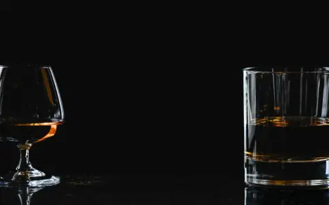 Kieliszek z brandy i szklanka z whisky na ciemnym tle.