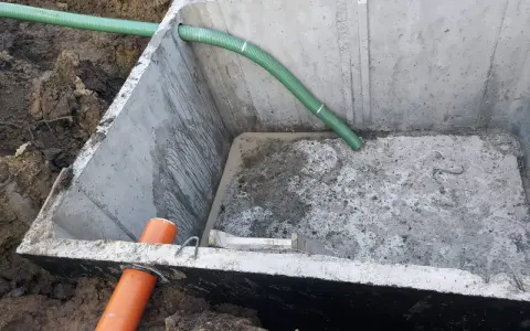 Montaż szamba betonowego 10m3. Widoczny betonowy zbiornik w wykopie, z podłączonymi rurami.