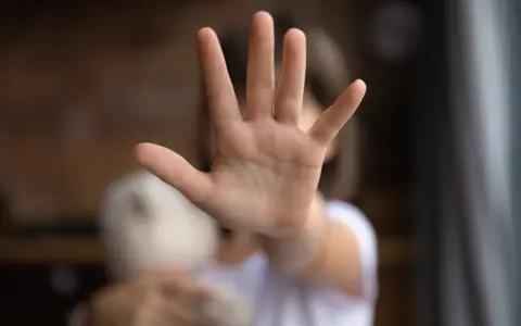 Main d'enfant tendue en signe d'arrêt, tenant une peluche.
