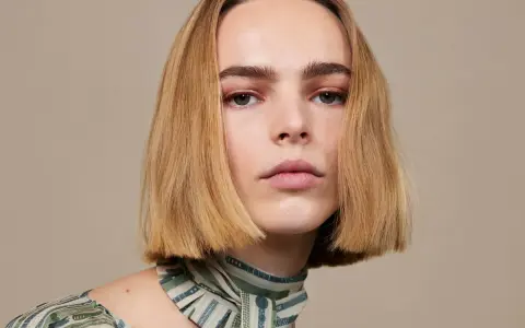 Modelka z subtelnym makijażem i fryzurą bob krótki tył, prezentuje się elegancko w bluzce z wzorem.