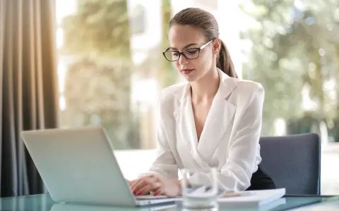 Kobieta w okularach pracuje na laptopie, szukając informacji, jak założyć działalność nierejestrowaną.
