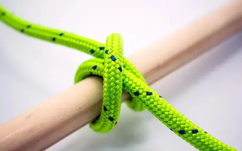 Jasnozielona lina z niebieskimi kropkami tworzy węzeł płaski na drewnianym patyku.