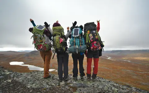 Quatre randonneurs, sacs à dos prêts, contemplent un paysage sauvage. Leur équipement, incluant des panneaux solaires, suggère une préparation pour une liste matériel randonnée 5 jours.
