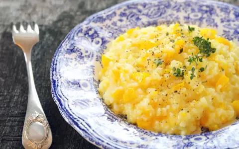 Pyszny, kremowy ryż do risotto z kawałkami dyni, posypany świeżym tymiankiem i pieprzem. Obok leży ozdobny widelec.