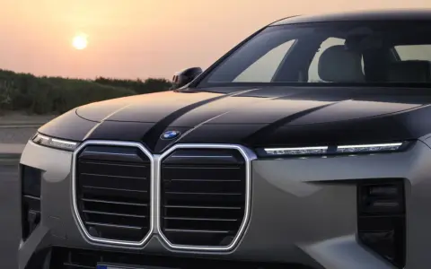 Przód luksusowego BMW M7 z podświetlaną atrapą chłodnicy i nowoczesnymi światłami, na tle zachodzącego słońca.