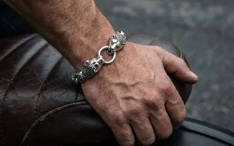 Męska dłoń z bransoletą z lwimi głowami, symbolizującą gest, kiedy mężczyzna daje kobiecie biżuterię.