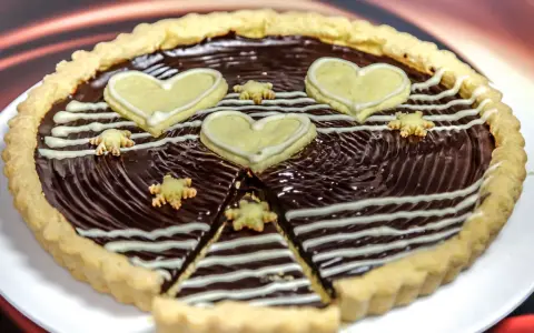 Una deliziosa crostata al cioccolato, decorata con cuori e fiorellini di pasta frolla, pronta per essere gustata.
