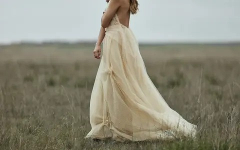 Braut in einem fließenden, cremefarbenen Kleid mit Tupfenmuster, das perfekt zum **dresscode boho hochzeit** passt. Sie steht in einer weiten, grasbewachsenen Ebene.