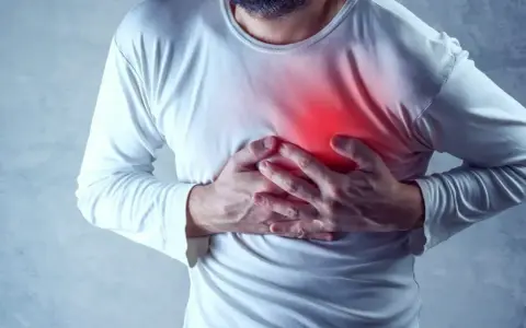 Mężczyzna trzyma się za klatkę piersiową, gdzie widoczny jest czerwony obszar bólu.