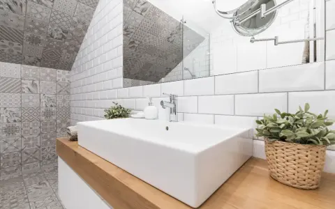 Salle de bain moderne avec lavabo rectangulaire, robinetterie chromée et un mur orné de **pose carrelage mural** patchwork gris et blanc.