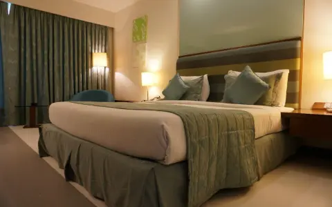 Ideas de iluminación para dormitorio de matrimonio: cama acogedora con lámparas de noche y cortinas verdes.
