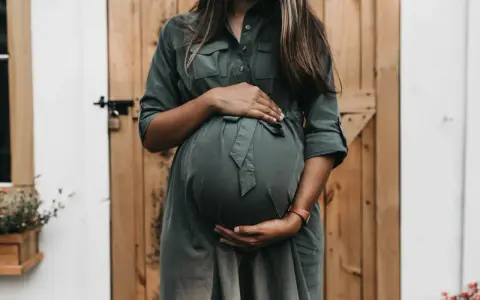 Kobieta w zielonej sukience obejmuje ciążowy brzuch. Czy to tokofobia co to?