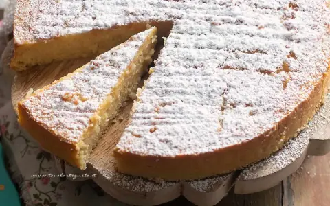 Una deliziosa torta di riso, cosparsa di zucchero a velo, su un tagliere di legno. Una fetta è già stata servita.