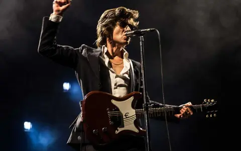 Alex Turner från Arctic Monkeys, med knuten näve i luften, spelar gitarr på scen i Stockholm.