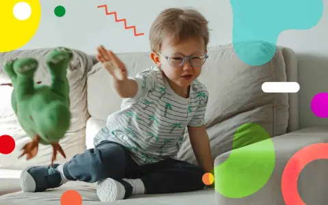 Un bambino super attivo gioca sul divano con un pupazzo verde. Le sue mani sono in movimento, pronto a interagire con il giocattolo.