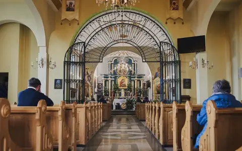 Wnętrze sanktuarium Matki Bożej Pięknej Miłości w Polańczyku. Wierni siedzą w ławkach, patrząc na ołtarz.