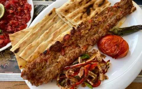 Pyszne tureckie jedzenie: kebab z mięsa mielonego, grillowany pomidor, papryka i świeże pieczywo. Obok sałatka z pomidorów.