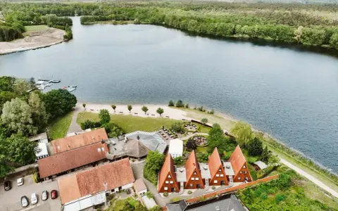 Idyllischer Seeuferbereich mit Sandstrand, Booten und Häusern. Ein perfekter Ort für einen entspannten Seeurlaub in Gronau.