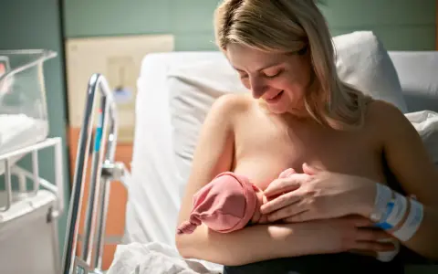 Uśmiechnięta mama karmi piersią noworodka. Pierwsze krople siary z piersi to cenny początek dla maluszka.