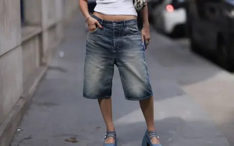 A person in denim bermuda shorts and a white crop top sports chunky blue platform Mary Janes, a nod to early 2000s shoe trends.