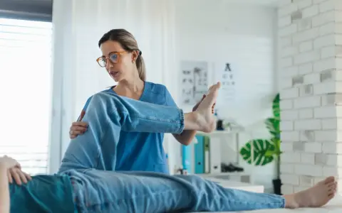 Fizjoterapeutka bada nogę pacjenta. Czy do fizjoterapeuty potrzebne jest skierowanie? Zależy od placówki.