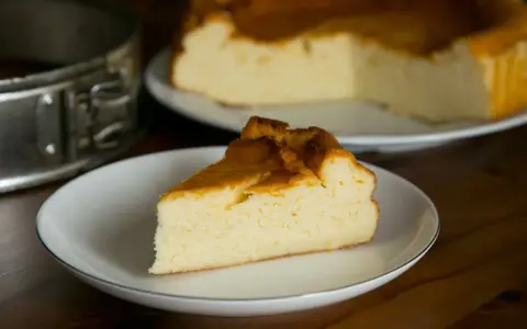 Puszysty sernik z mlekiem skondensowanym, z rumianą skórką, na talerzyku. Obok forma do pieczenia.