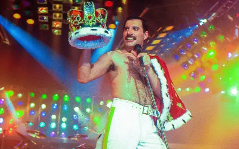 Freddie Mercury, król sceny, w koronie i z mikrofonem, na tle kolorowych świateł.