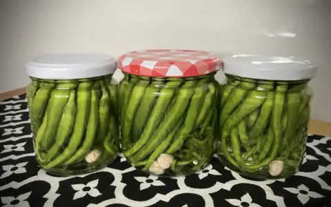 Tres frascos de vidrio llenos de piparras en vinagre, con ajos en el fondo. Uno tiene tapa a cuadros rojos y blancos.
