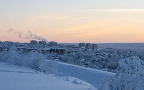 Vinterlandskap i lapponia svedese med snötäckta träd och byggnader i fjärran under en rosa solnedgång.