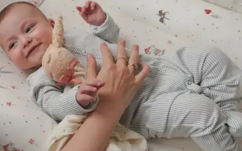 Uroczy niemowlak w pajacyku leży w łóżeczku. Dowiecie się, jak ubrac dziecko do spania, by było mu wygodnie.