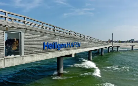 Hol dir die besten heiligenhafen tipps! Die Seebrücke mit dem Schriftzug "Heiligenhafen" ragt ins grüne Meer.