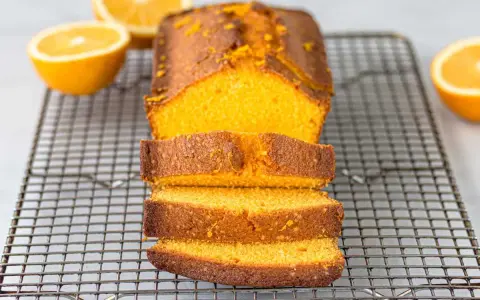 Un delicioso bizcocho de naranja, recién horneado y cortado en rebanadas, reposa sobre una rejilla.