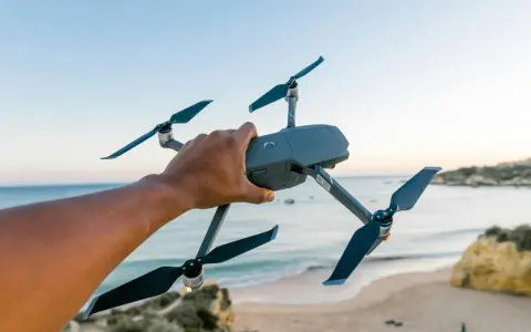 Hand hält Drohne über Strand. Bereit für Aufnahmen in Deutschland, vielleicht für eine Notam-Meldung.