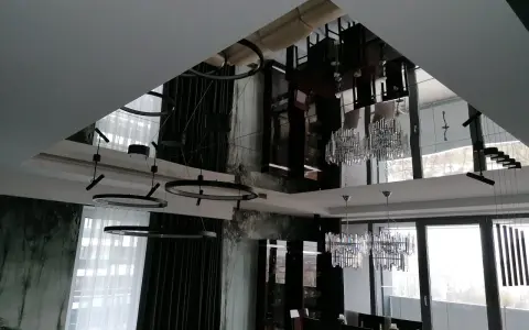 Eleganckie lustro na suficie w sypialni odbija nowoczesne lampy i meble, tworząc wrażenie przestronności.
