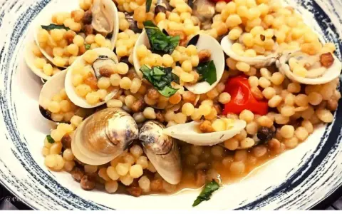 Piatto di fregola con vongole, pomodorini e basilico fresco. Un classico sardo che profuma di mare.