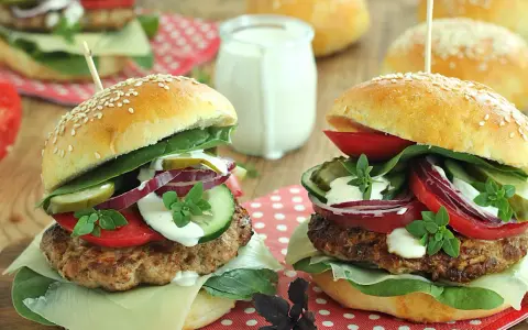 Dwa soczyste burgery wołowe z dodatkami na drewnianym tle.