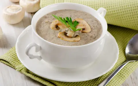 Un réconfortant velouté de champignon, garni de lamelles et d'une touche de persil, servi dans une tasse blanche sur une serviette verte.
