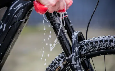 Mit Hausmitteln das Fahrrad sauber machen: Eine Hand mit rotem Schwamm reinigt den Rahmen und die Federgabel, Schaum und Wasser spritzen.