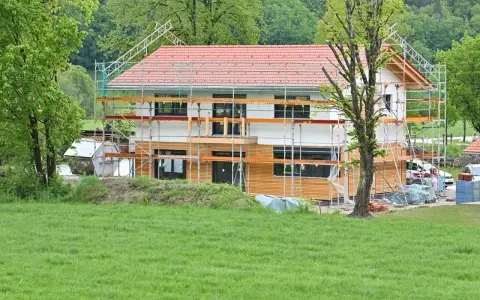 Ein Haus im Bau, umgeben von Gerüsten. Man sieht, wie man ein Haus baut, mit Holzfassade und rotem Ziegeldach.