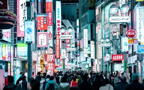 Eine belebte Straße mit vielen leuchtenden Neonschildern, die Geschäfte und Restaurants bewerben. Dies ist ein typisches Beispiel für einen urbanen Raum, voller Leben und Aktivität.