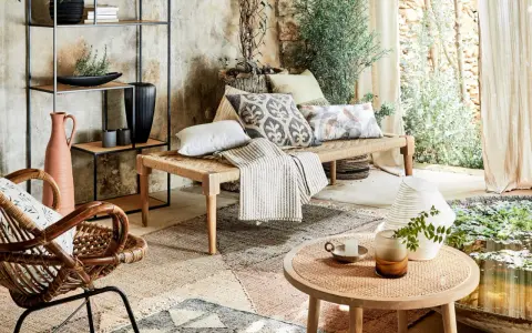 Un salon sans canapé, avec un banc tressé, des coussins décoratifs, un fauteuil en rotin et une étagère murale.