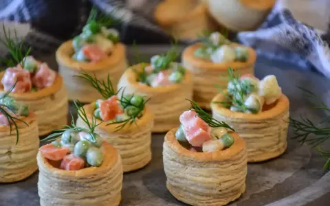 Plusieurs bouchées à la reine garnies d'une salade crémeuse de petits pois, carottes et jambon, décorées d'aneth.