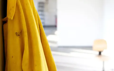 Gelbe Regenjacke hängt an einer Wand, bereit für die Regenjacke reparieren. Flecken auf dem Stoff deuten auf vergangene Abenteuer hin.