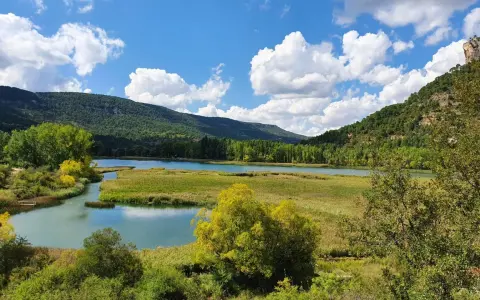 Paisaje de lagunas y montañas verdes, ideal para rutas senderismo Cuenca. Cielo azul con nubes blancas.