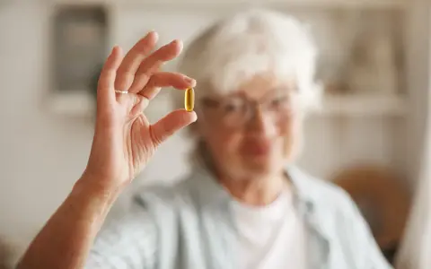 Anziana con occhiali tiene una capsula gialla tra pollice e indice. Chiediti: deursil quando prenderlo per il tuo benessere.