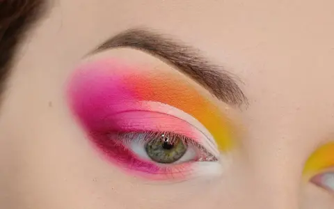 Oko z intensywnym makijażem w stylu cut crease, łączącym odcienie różu, pomarańczy i żółci.