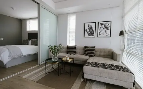 Nowoczesny salon z przesuwnymi drzwiami, za którymi widać sypialnię. Sofa, stoliki, obrazy.