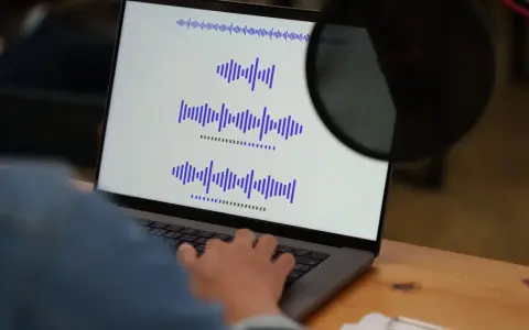 Osoba pracuje przy laptopie, na ekranie widoczne są wykresy fal dźwiękowych, co może być związane z tworzeniem adlibów.
