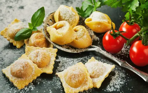 Świeże ravioli i tortellini, posypane cukrem pudrem, z pomidorkami koktajlowymi i bazylią. Idealne z czym podawać ravioli? Z prostym sosem!